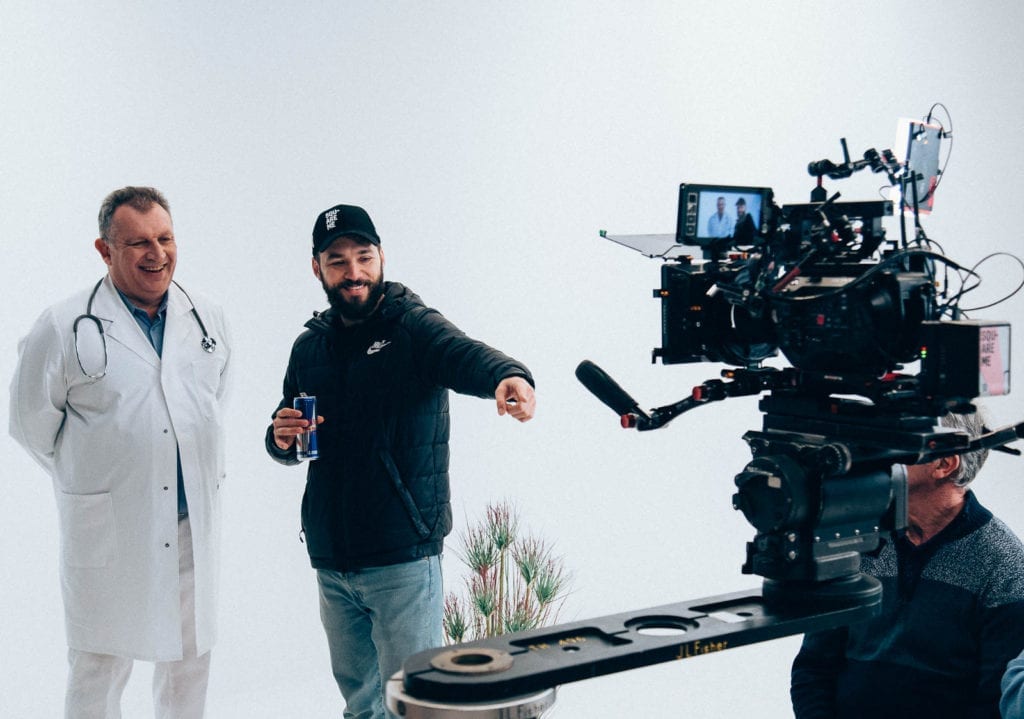 Squareme Mesi medical devices video - director Luka Štigl with actor Scott Alexander Young in a doctor's uniform standing on set in front of the camera in a white studio