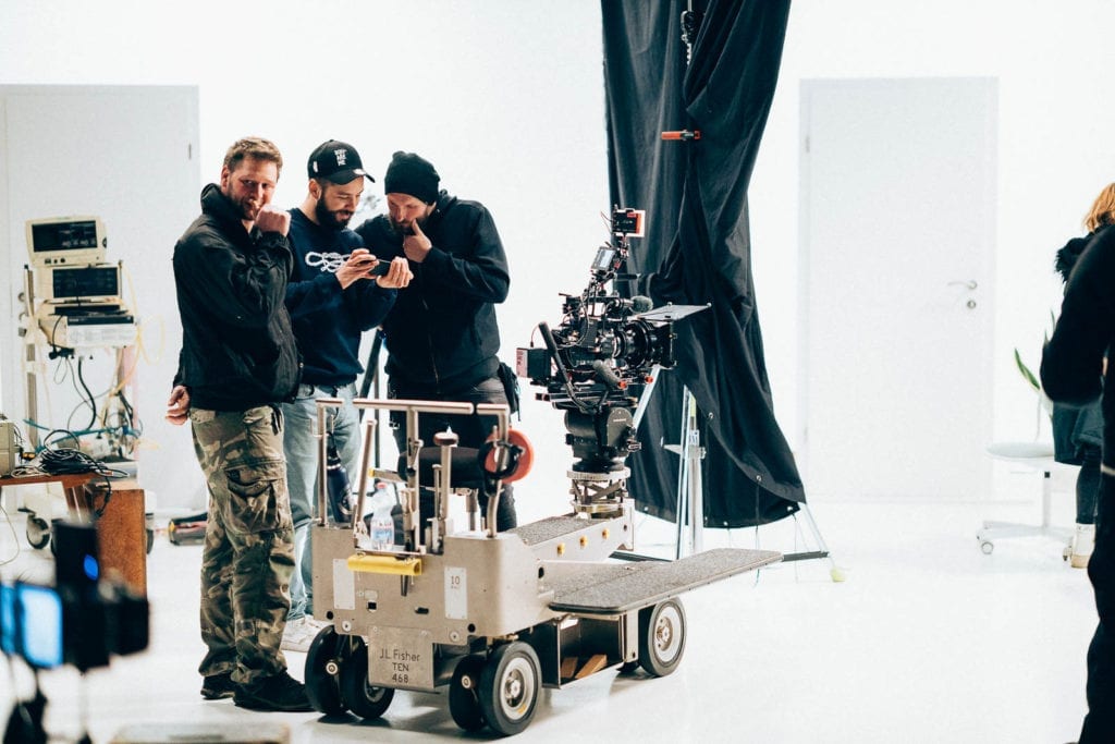 Squareme Mesi medical devices video - DOP Dominik Istenič and director Luka Štigl looking at a phone on set in a white studio with dolly cart with a mounted camera in front and old medical devices in the background